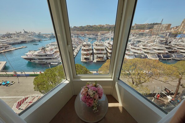 A view from a window overlooking a marina with yachts and boats docked, a flower vase on the windowsill, and a clear sky. - Hotel Port Palace (Monaco)