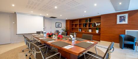 A conference room with a long table, chairs, a projector screen, and a bookshelf.