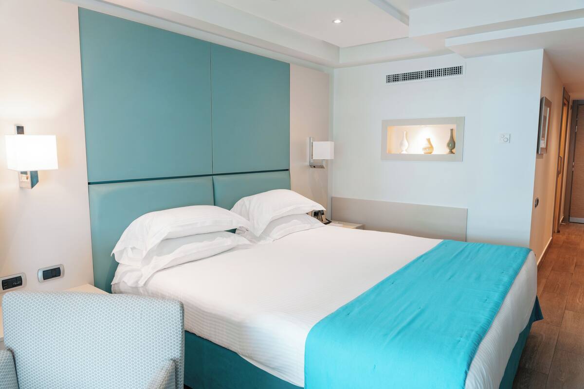 Ein Hotelzimmer mit einem großen Bett, einem Kopfteil, Nachttischlampen, einem kleinen Tisch und einem Sessel.