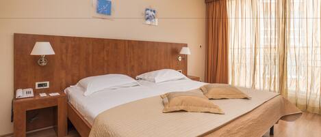 A hotel room with a large bed, two bedside tables, a telephone, and a window with curtains.