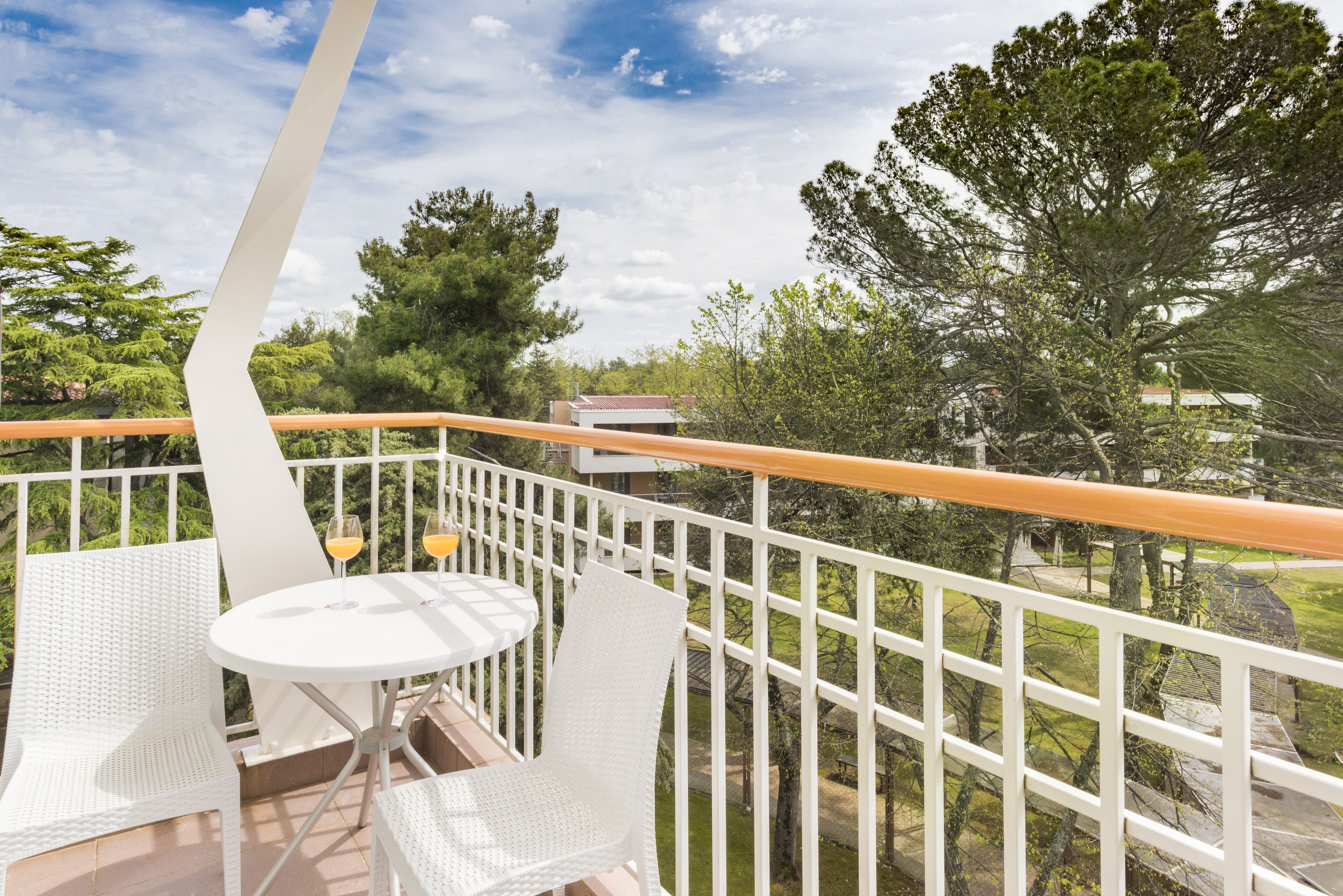 A balcony with white wicker furniture, a table, and two glasses of orange juice.