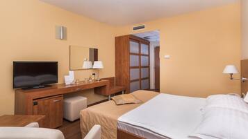 A hotel room with a bed, a desk with a television, a chair, a small table, and a mirror.