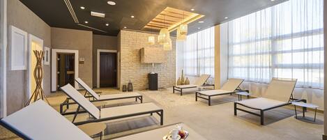 Un espacio lounge moderno con sillones, una pared de piedra y un gran ventanal que proporciona luz natural.