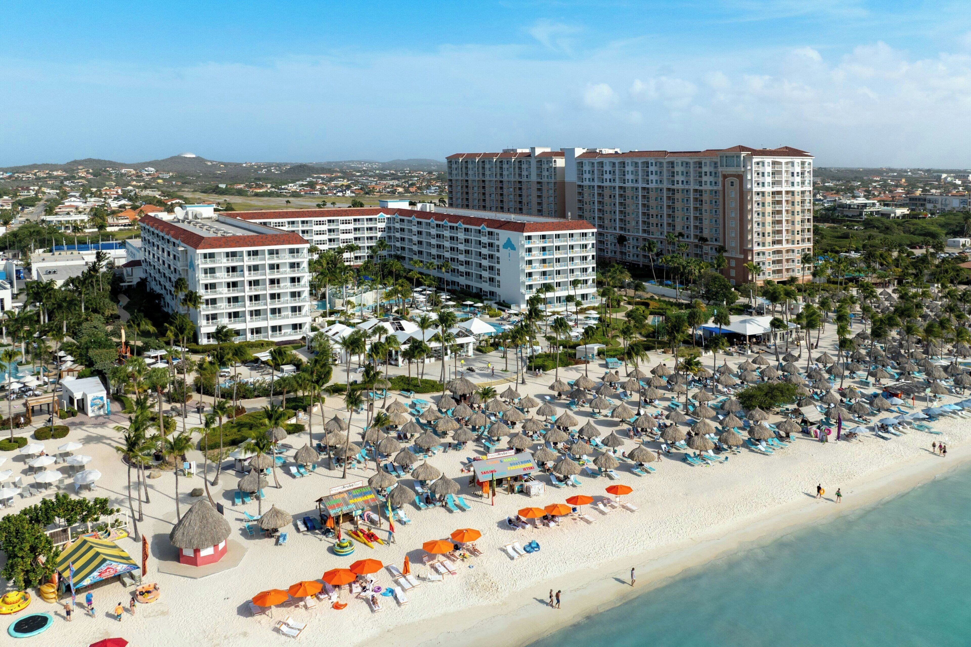 A resort with multiple hotel buildings, a beach with umbrellas and lounge chairs, and a clear view of the coastline.