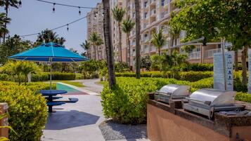 A resort courtyard with outdoor seating, a barbecue grill, and a swimming pool.