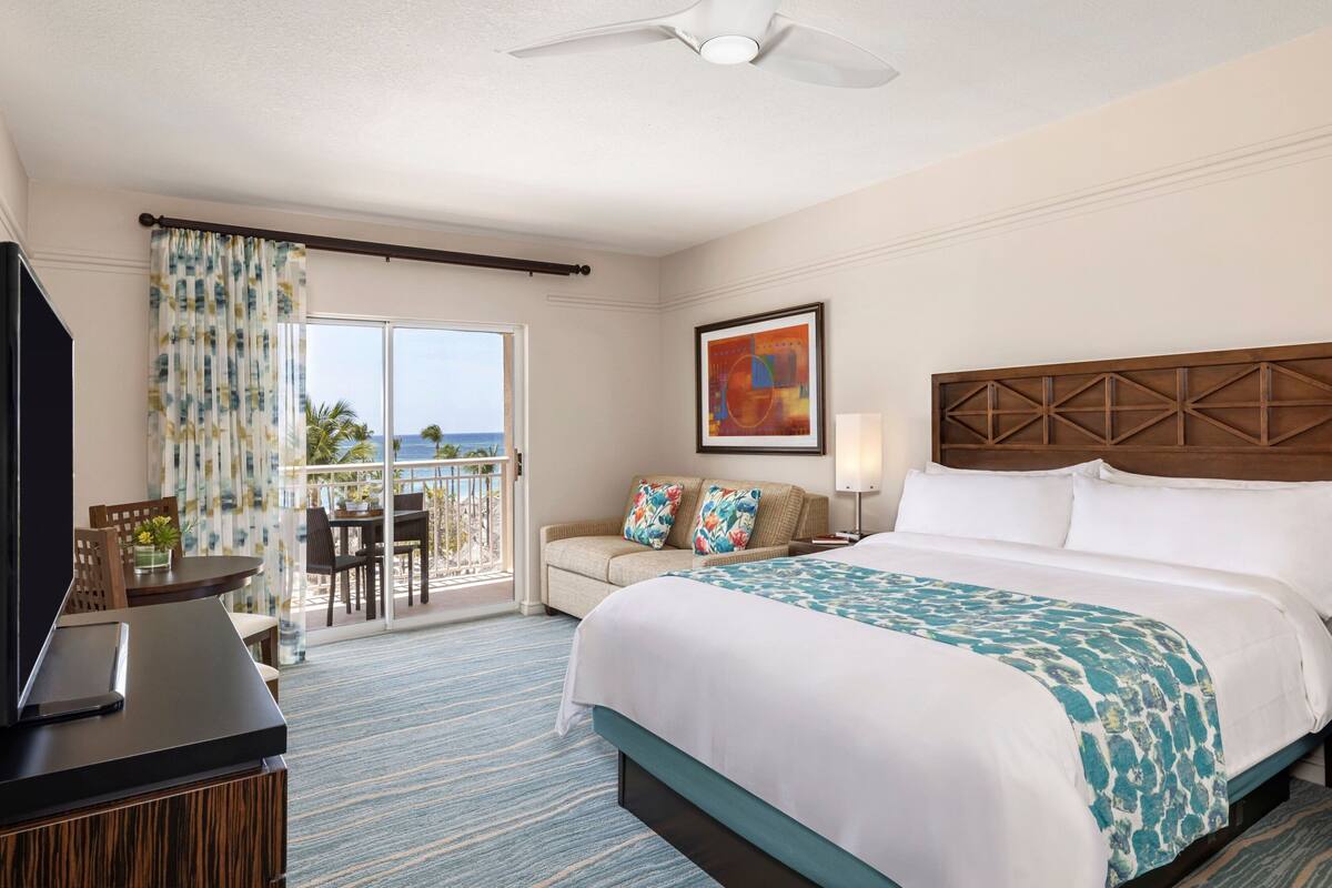 A hotel room with a bed, a desk, a chair, a TV, and a balcony with a view.