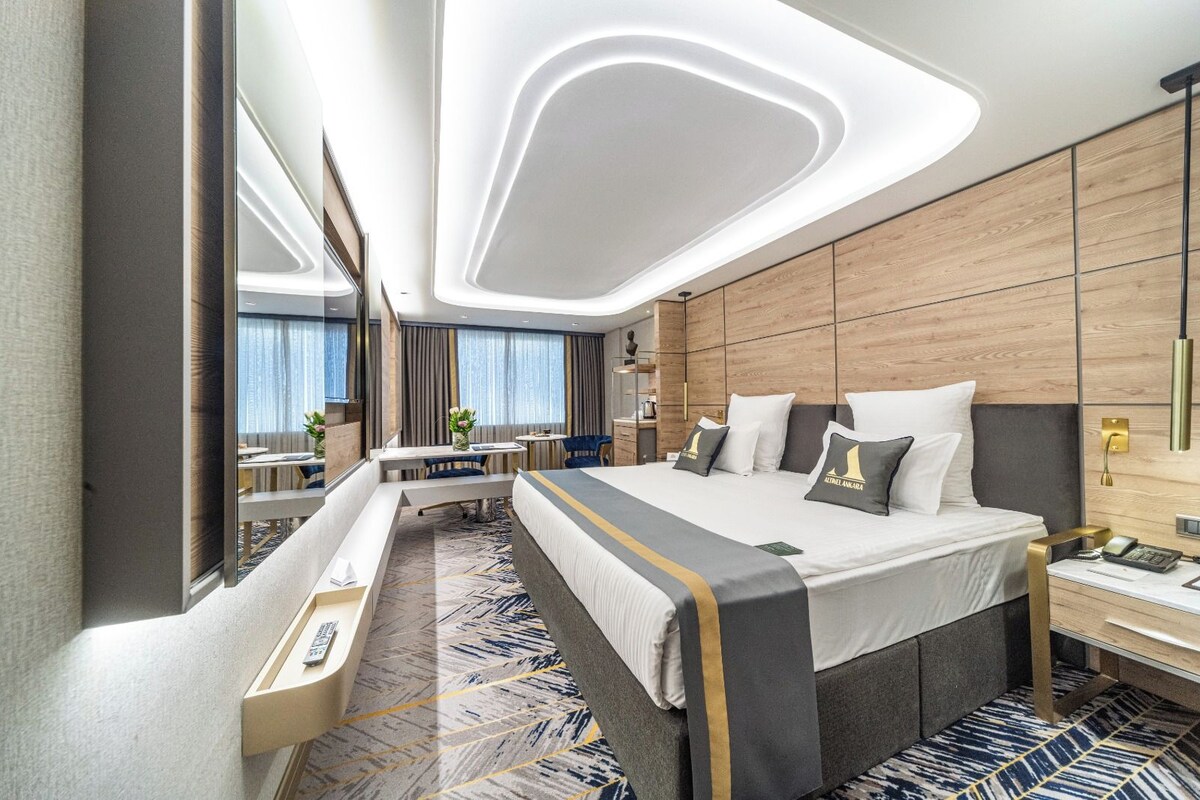 Una habitació d'hotel moderna amb un llit gran, un escriptori, un mirall i vista a la ciutat.