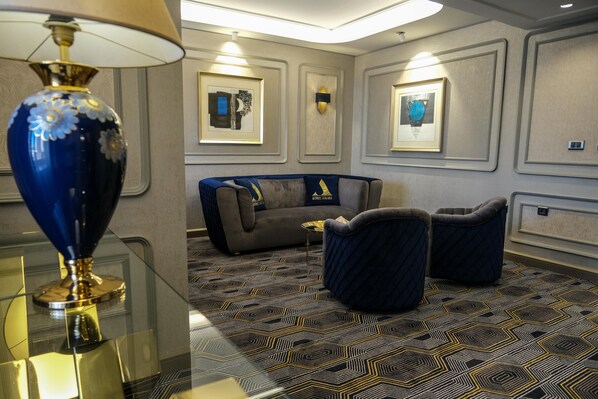 A hotel lobby with a patterned carpet, a sofa, two armchairs, a decorative lamp, and framed artwork on the walls. - Altınel Ankara Hotel & Convention Center (Ankara)