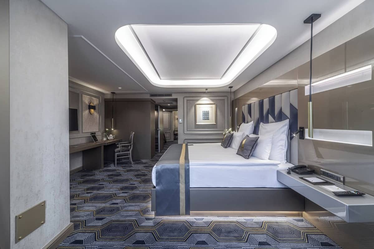 A modern hotel room with a large bed, a desk, and a seating area.
