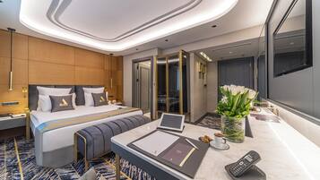 Una habitación de hotel moderna con una cama grande, mesitas de noche, un escritorio con una computadora portátil, un teléfono y un florero con flores.