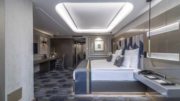 A modern hotel room with a large bed, bedside tables, a desk, and a seating area.