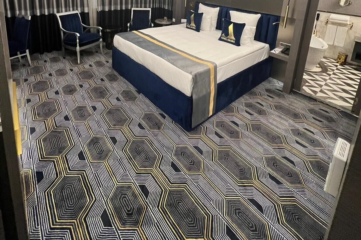 Ein modernes Hotelzimmer mit einem großen Bett, einer Sitzecke mit Stühlen, einem Badezimmer und einem Boden mit geometrischem Muster.