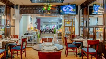 A restaurant with multiple dining tables and chairs, a ceiling fan, and televisions mounted on the walls.