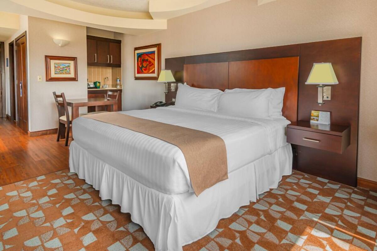 Une chambre d’h ôtel avec un grand lit, un bureau et une chaise. Il y a deux lampes sur les tables de chevet.