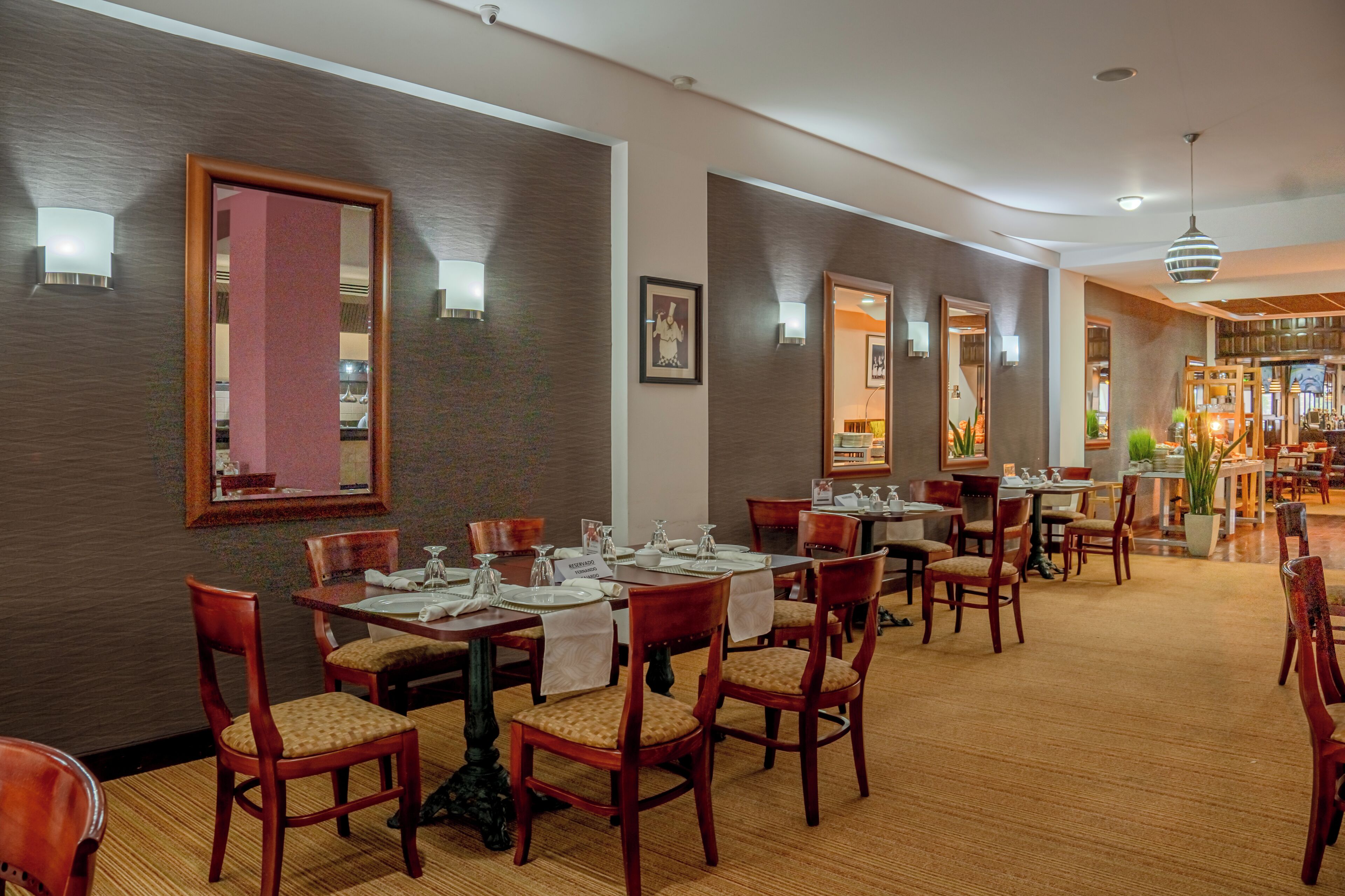 Een restaurant in een hotel met houten tafels en stoelen, een vloerkleed en wandlampen.
