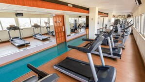 A gym with treadmills, a mirrored wall, and a pool area.