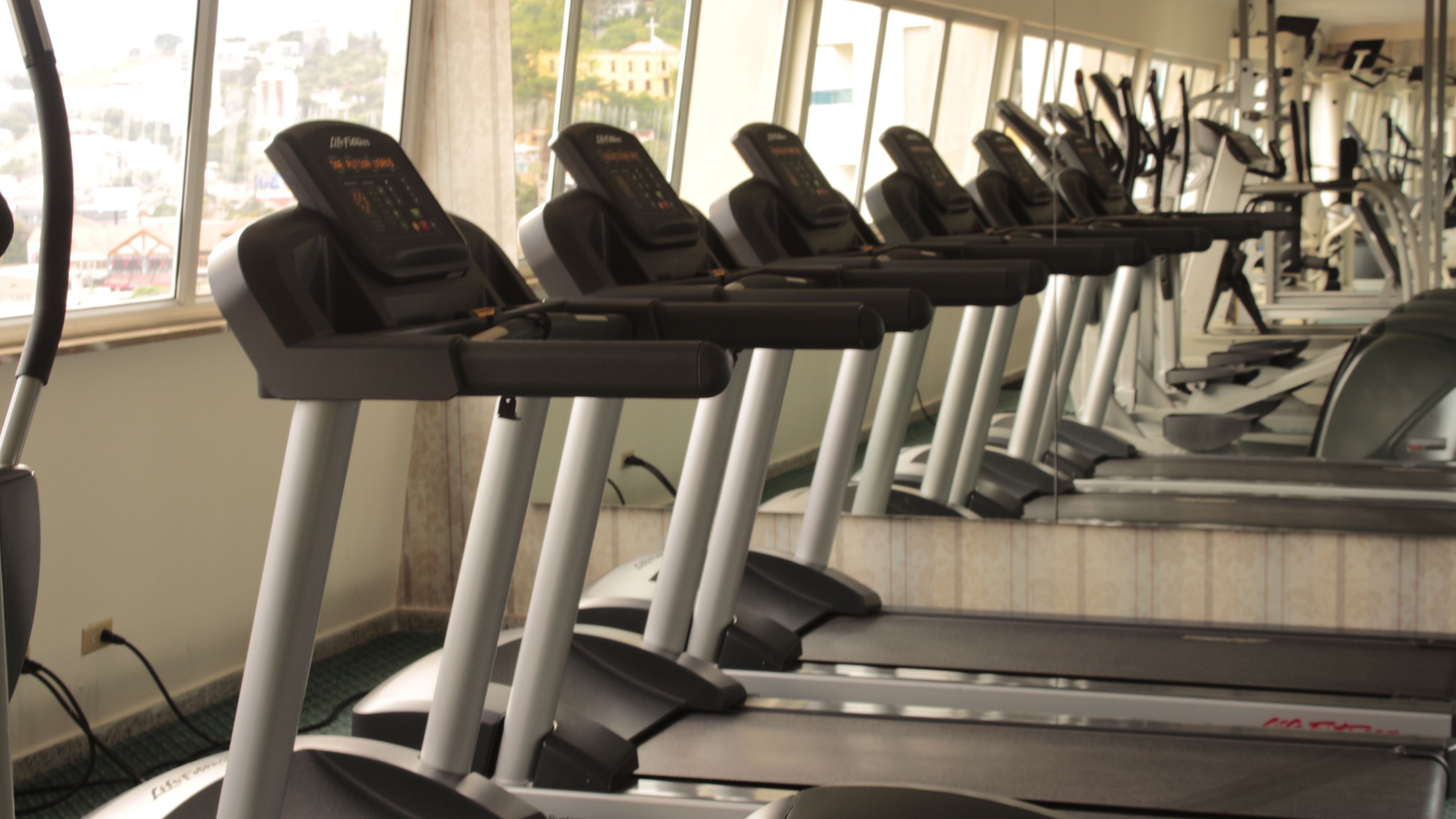 Varias cintas de correr en un gimnasio, con vistas a edificios a través de la ventana.