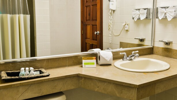 A bathroom with a sink, a mirror, a towel dispenser, and a hairdryer. - Hotel Plaza San Martin (Tegucigalpa)