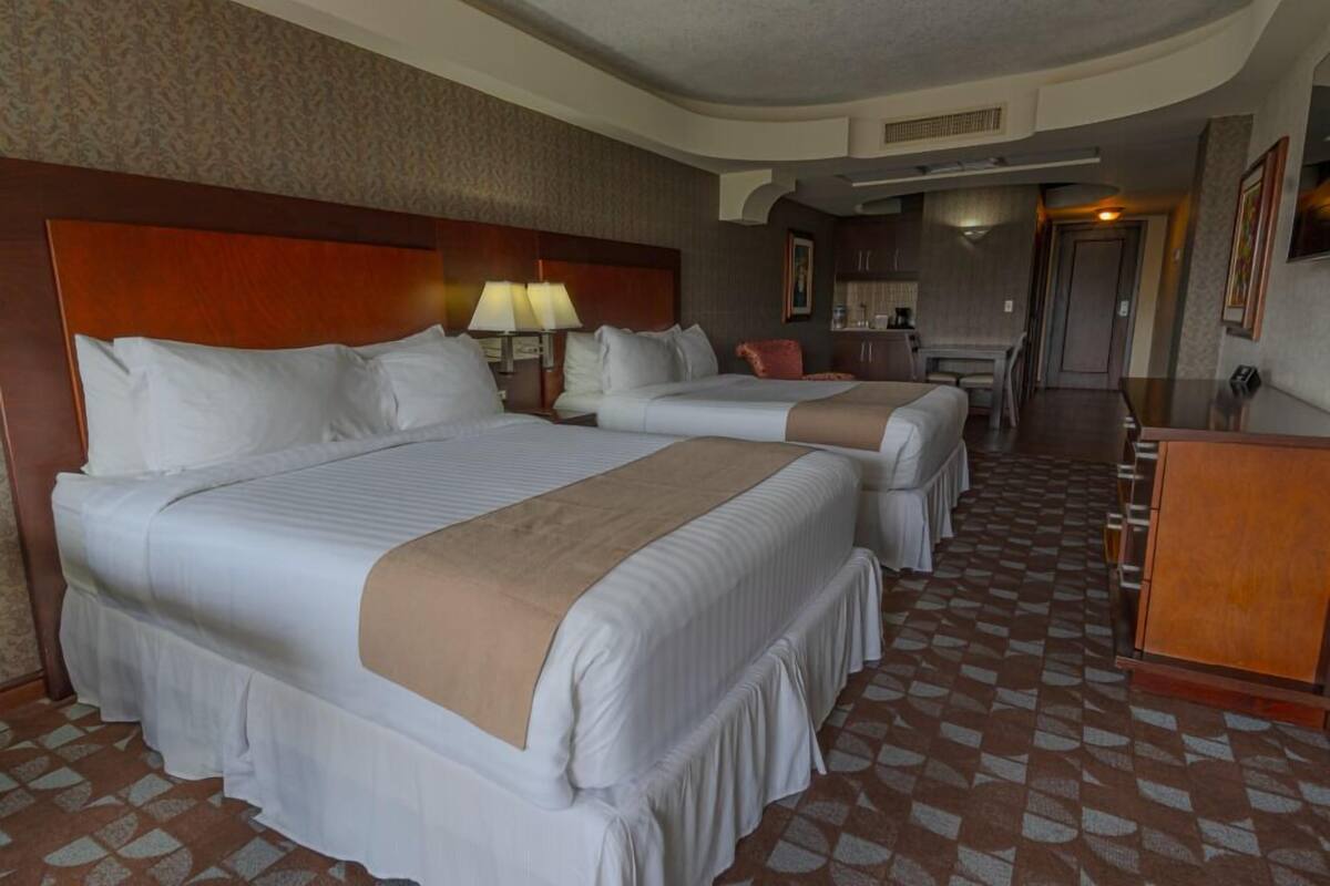 Une chambre d’hôtel avec trois lits, une tête de lit en bois, un bureau et un sol à motifs.