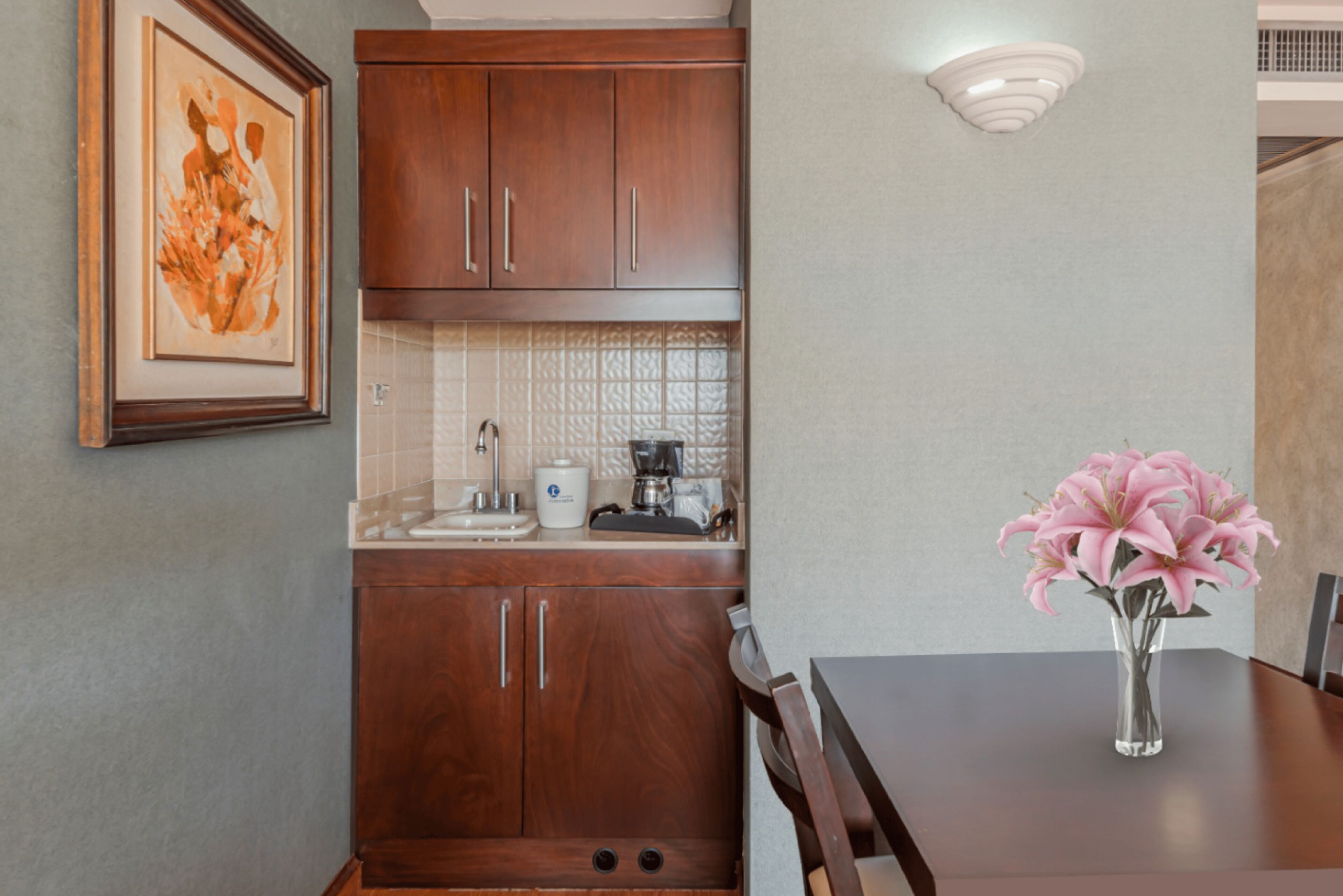 A kitchen with wooden cabinets, a coffee maker, and a vase with flowers on the table.