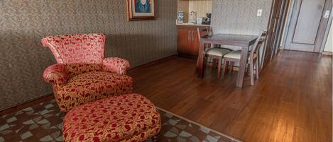 A room with a patterned carpet, a wooden dining table with chairs, and a red patterned armchair.