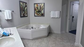 Une salle de bain avec une grande baignoire, un lavabo, deux tableaux encadrés et une porte donnant sur une autre pièce.
