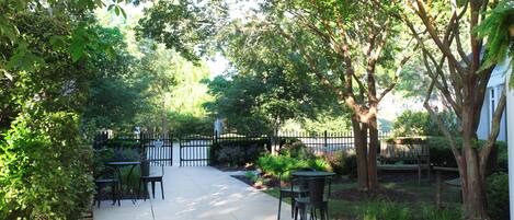 A patio area with tables and chairs, surrounded by greenery and a fence.