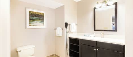 Un baño con inodoro, lavamanos, espejo y un cuadro en la pared.