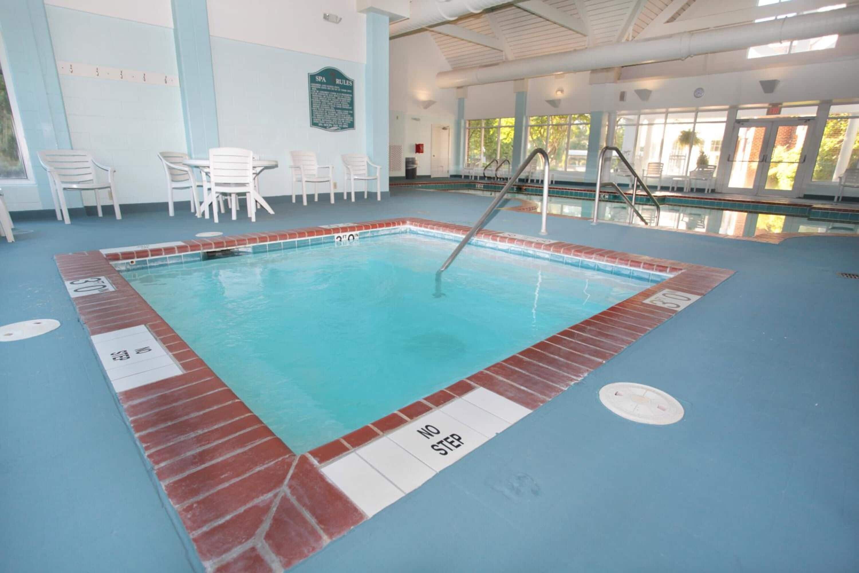 An indoor swimming pool with a 'NO STEP' zone, poolside chairs, and a 'SPA RULES' sign.