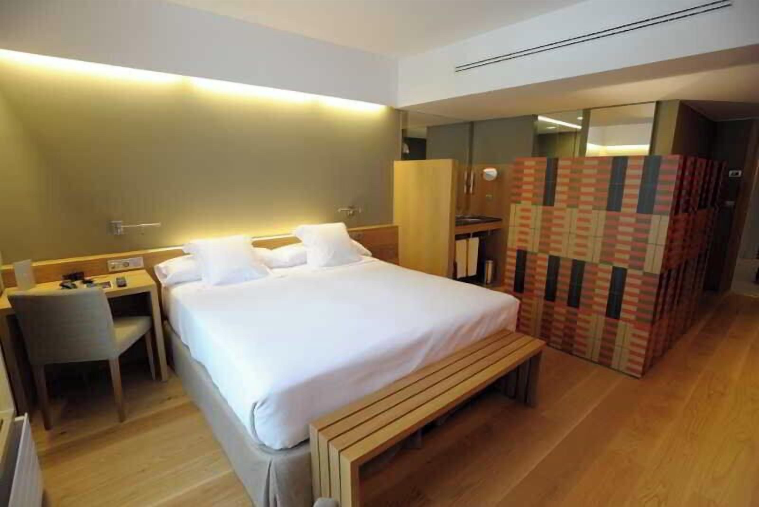 Ein Hotelzimmer mit Bett, Schreibtisch, Stuhl, Bank und Kleiderschrank.