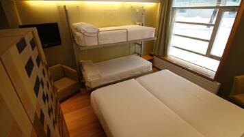 A bunk bed room with a flat-screen TV, a window with a view of the outside, and a wooden floor.