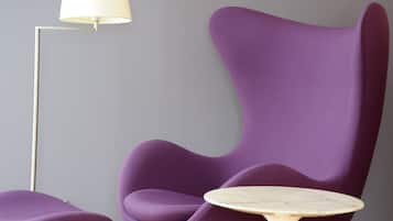 Un sillón morado con una mesa redonda a su lado, una lámpara de pie y una pared lisa.