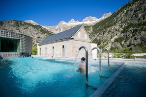 Une piscine avec un bâtiment en pierre et des montagnes en arrière-plan.