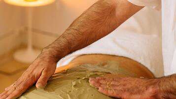 Iemand ontvangt een massage met een groene substantie op de rug.
