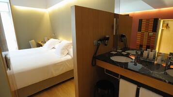 Habitación de hotel con cama, separador de madera, baño con lavabo y espejo.
