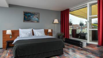Habitación de hotel con una cama grande, dos lámparas de noche, un cuadro en la pared y vista a un espacio exterior a través de una puerta corrediza de vidrio.