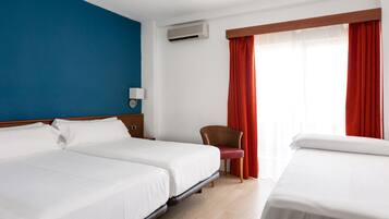 Habitación de hotel con dos camas, una silla, una mesita de noche, un equipo de aire acondicionado y una ventana con cortinas rojas.