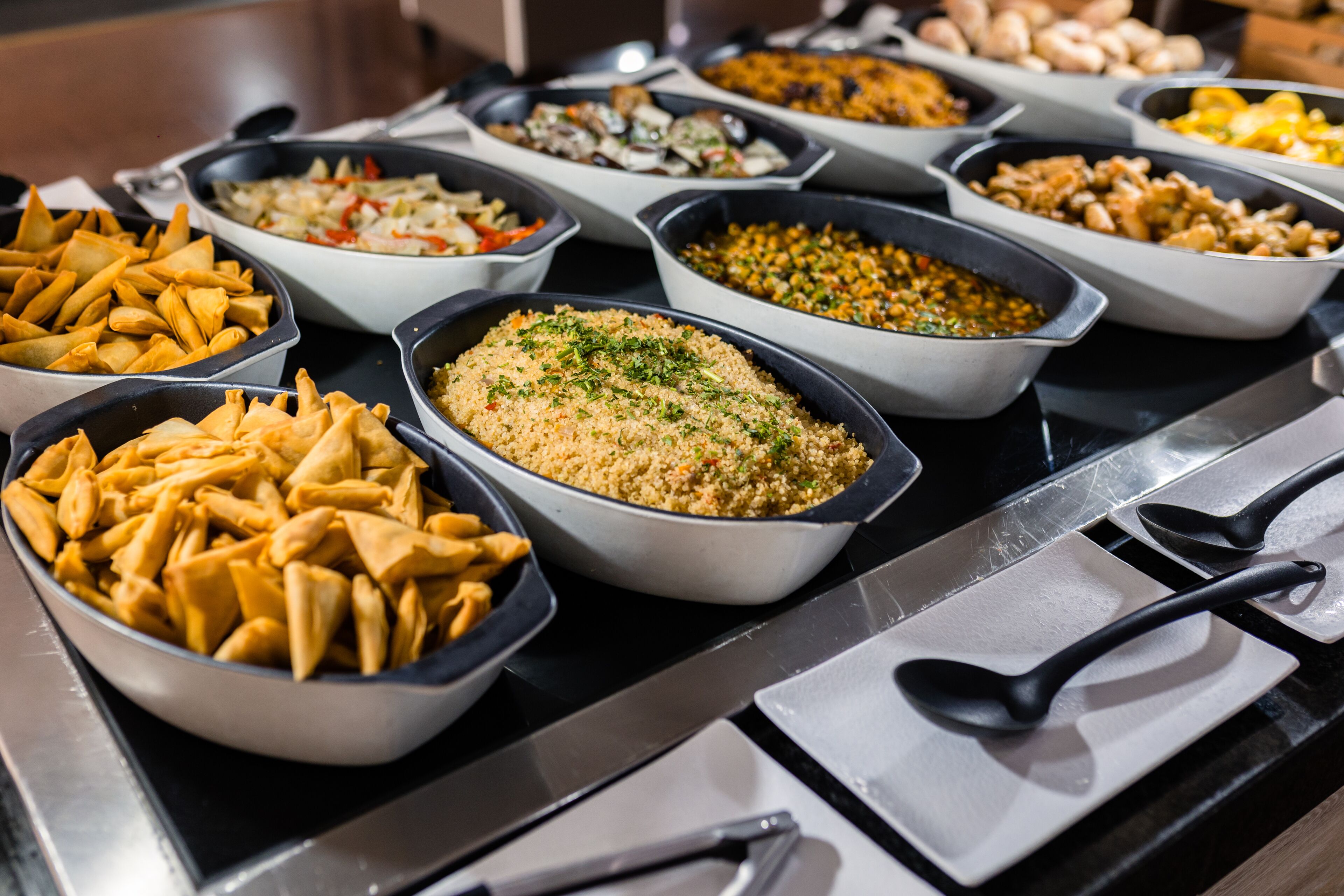 A buffet with various dishes including samosas, a couscous dish, and other mixed salads.