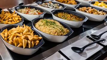 A buffet with various dishes including samosas, a couscous dish, and other mixed salads.