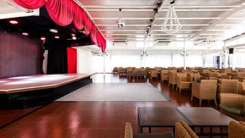 Un salón amplio con un escenario, filas de sillas y una cortina roja.