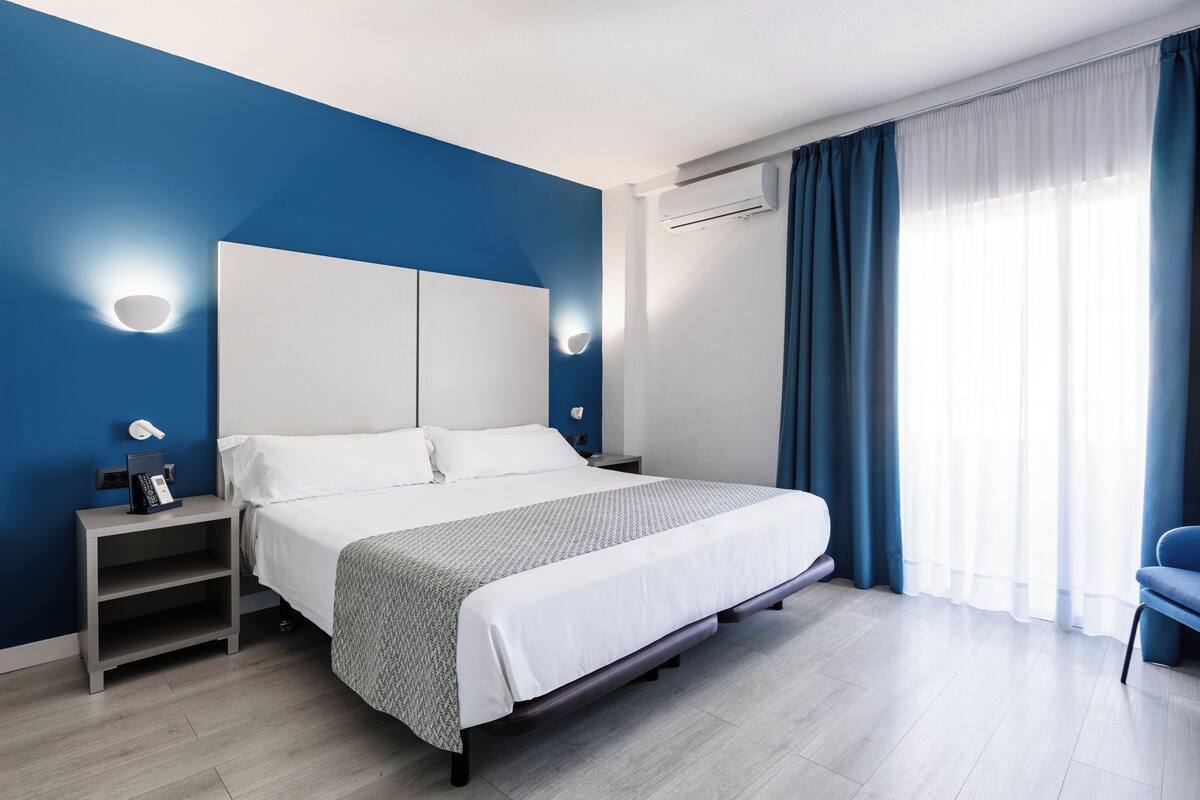 A modern hotel room with a large bed, bedside tables, and a nightstand.