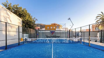 Una cancha de tenis interior con superficie azul, rodeada de vallas y un edificio con el logotipo de 'Tecnifibre' al fondo.
