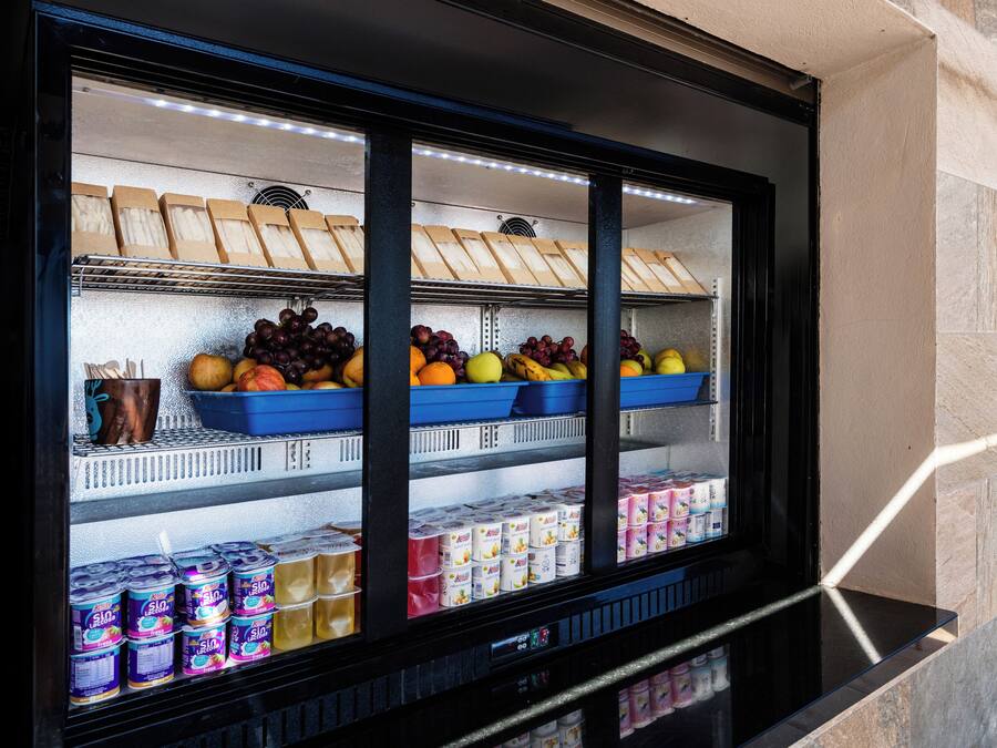 A refrigerated display case with various food items including fruits, cheeses, and dairy products.