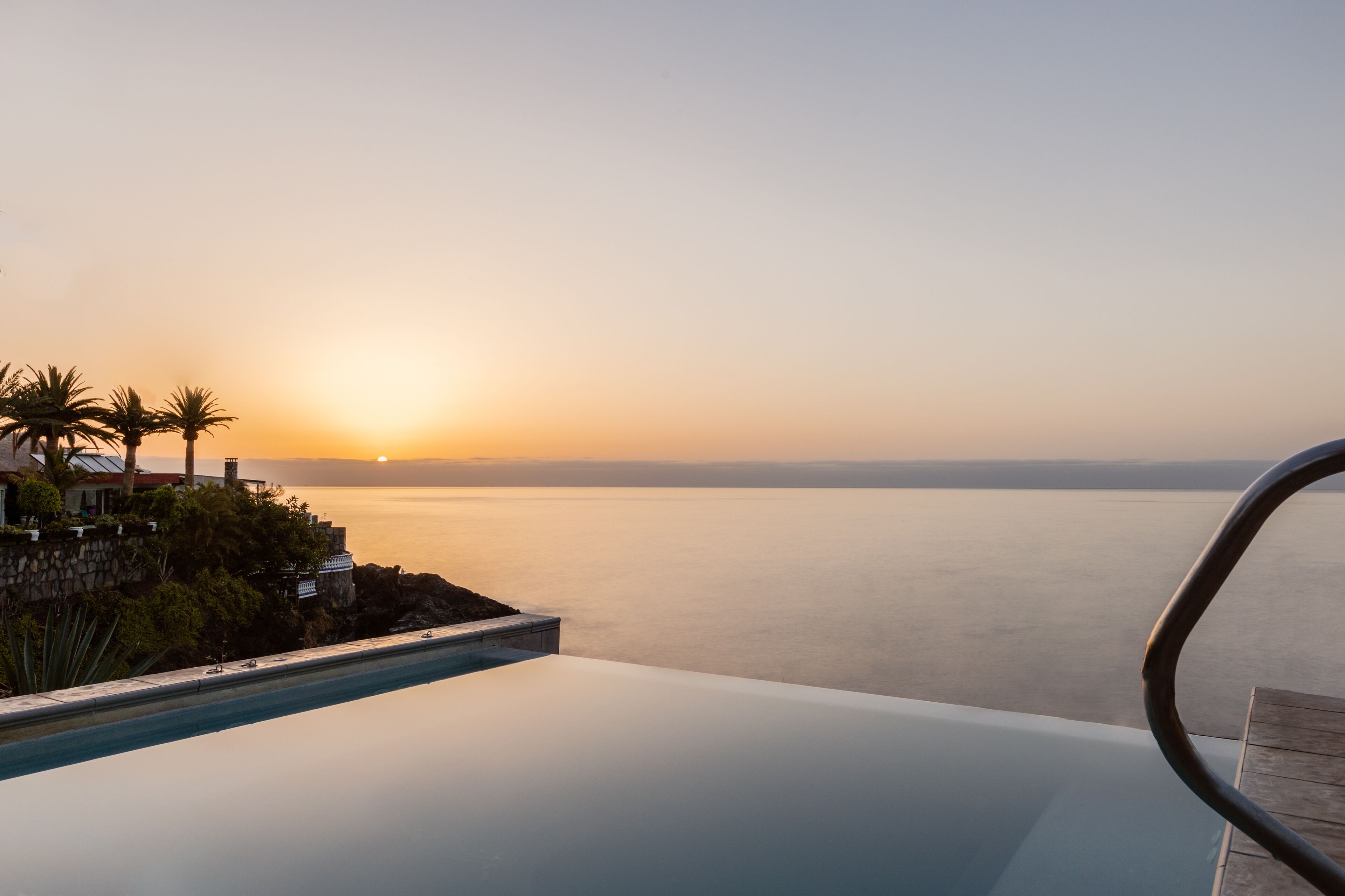 A luxurious infinity pool overlooking a calm sea at sunset.