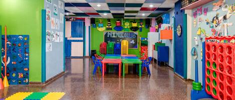 A colorful children's playroom with a checkered ceiling, a bulletin board with drawings, and a table with colorful chairs.