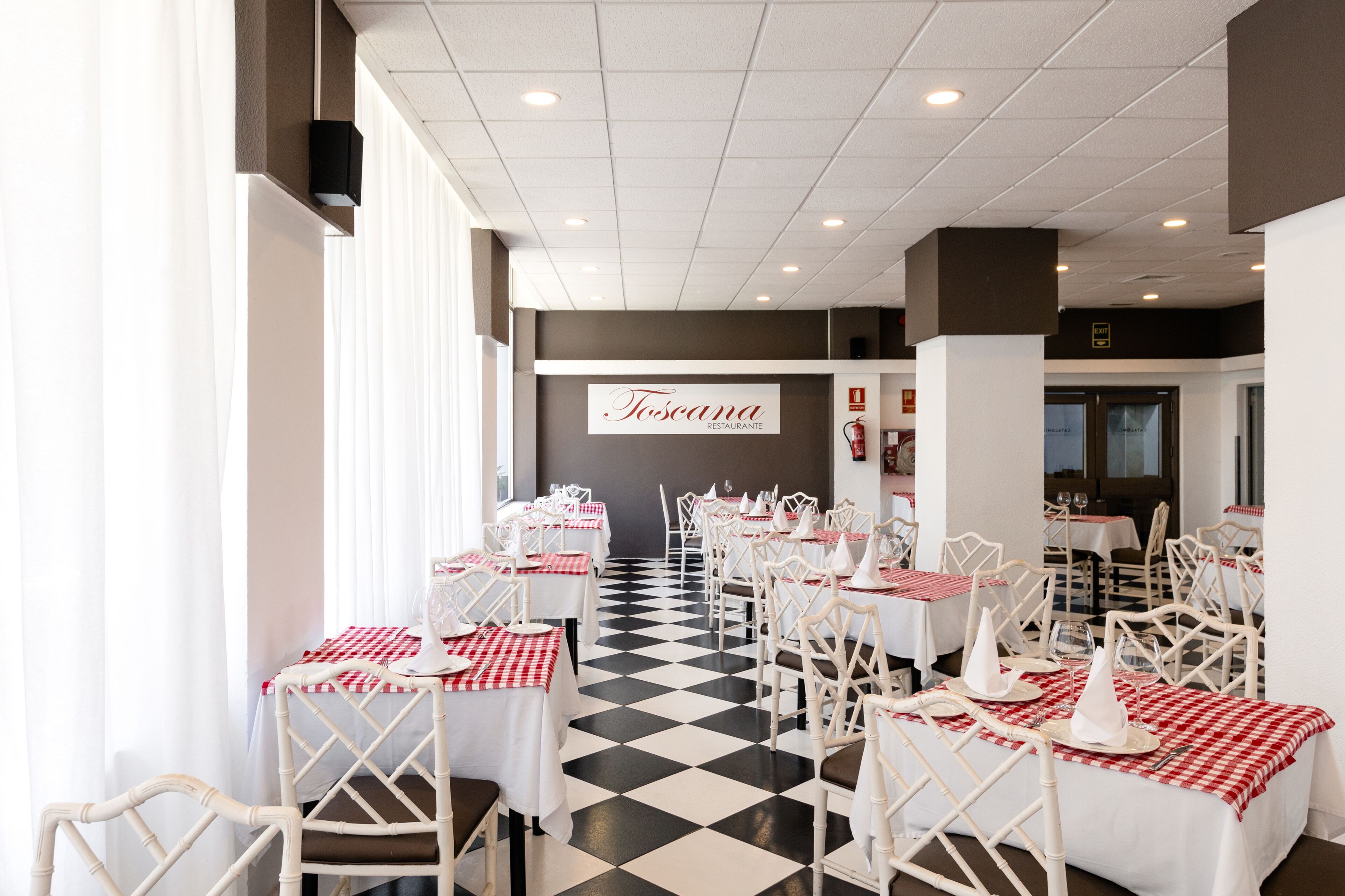 L’intérieur d’un restaurant avec des tables et des chaises blanches, des nappes à carreaux et un sol à carreaux noir et blanc.