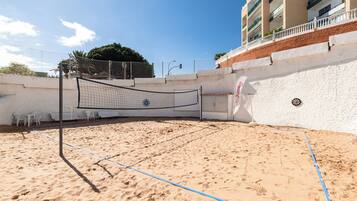 Una cancha de voleibol de playa con una red, sillas blancas y un edificio al fondo.