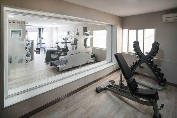 A modern gym with various exercise equipment, a large mirror, and a window with a view of the outside. - Catalonia Las Vegas - Adults Only (Puerto de la Cruz)