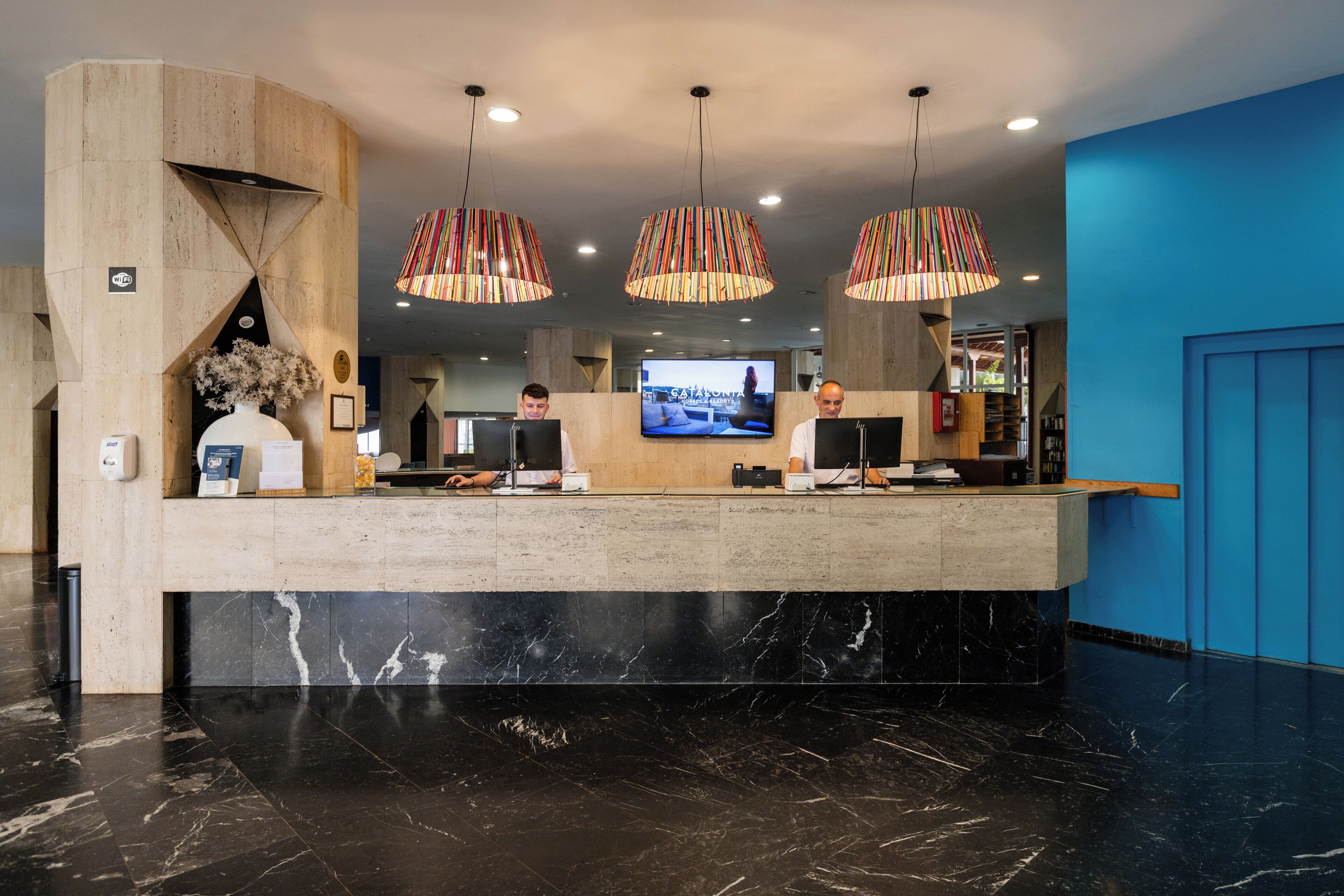 A reception desk with a marble base, a large flat-screen TV, and three striped pendant lights.