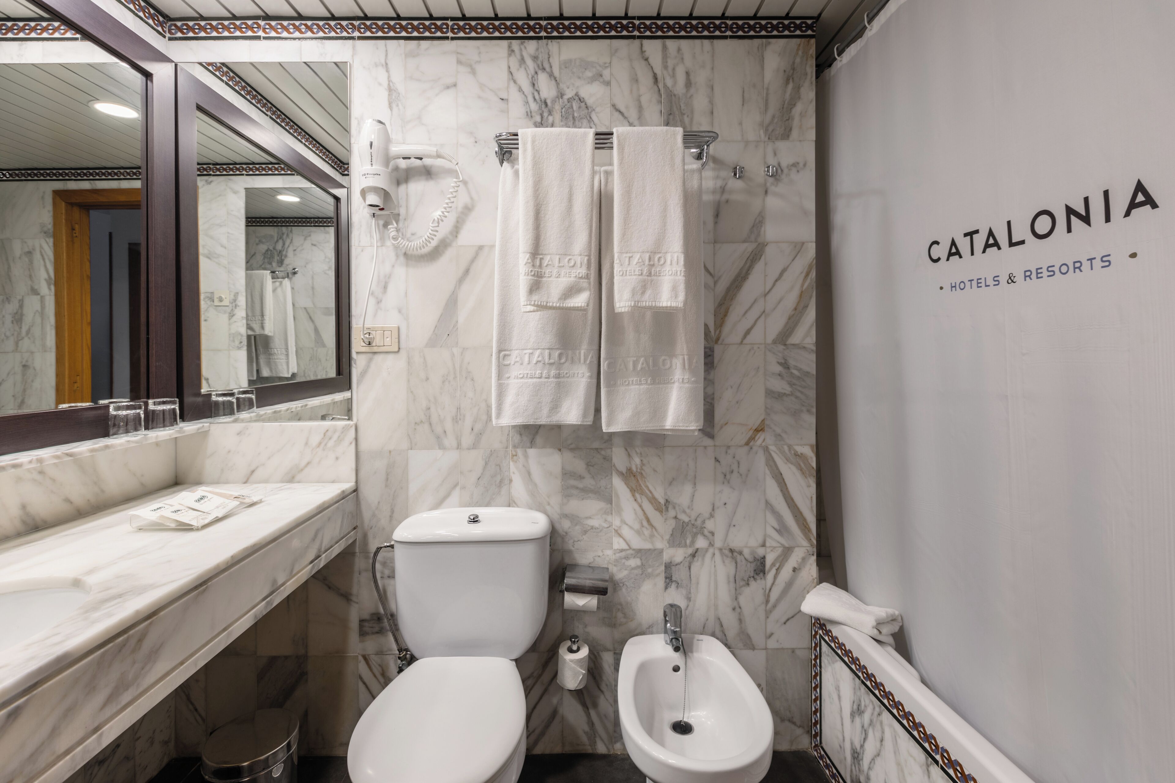 A bathroom with a marble wall, a toilet, a bidet, and a sink.